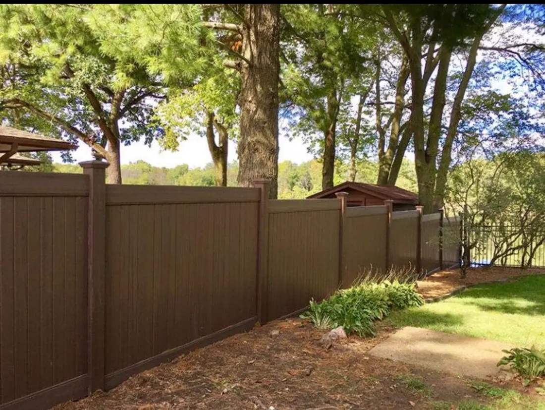 Brown wood-grain vinyl privacy fence along a wooded yard