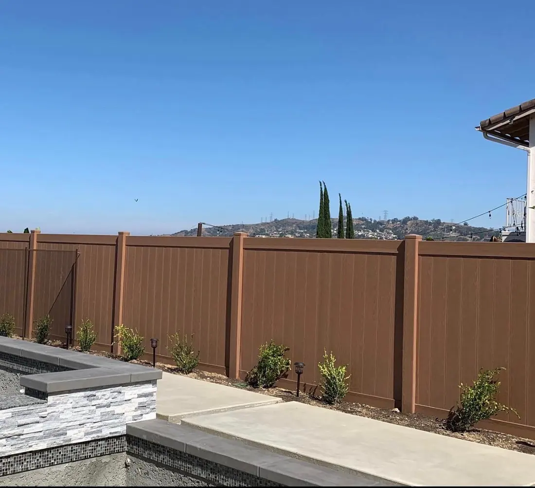 Brown wood-grain vinyl privacy fence beside a pool