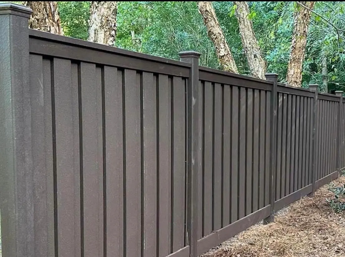Dark wood-grain vinyl privacy fence along a wooded property