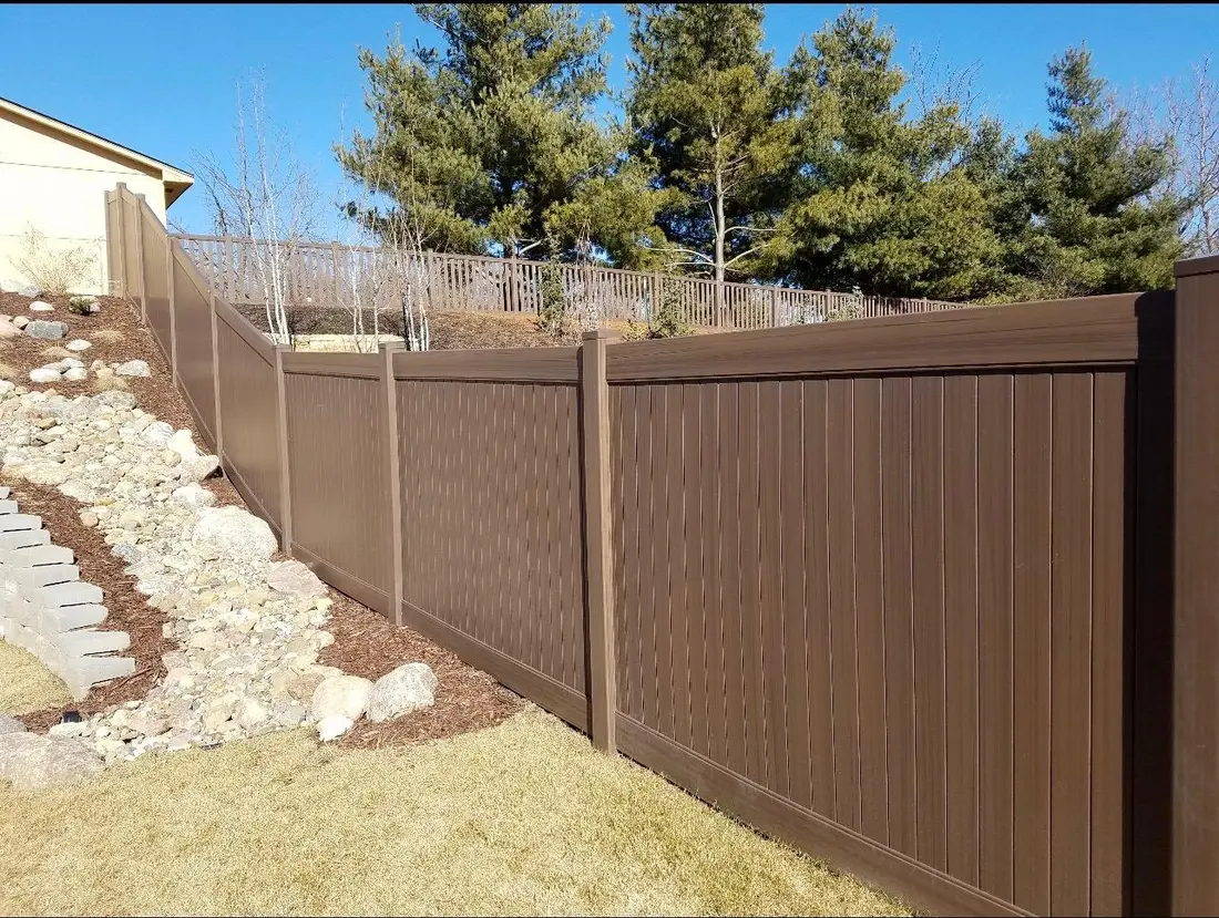 Dark wood-grain vinyl privacy fence on a sloped yard