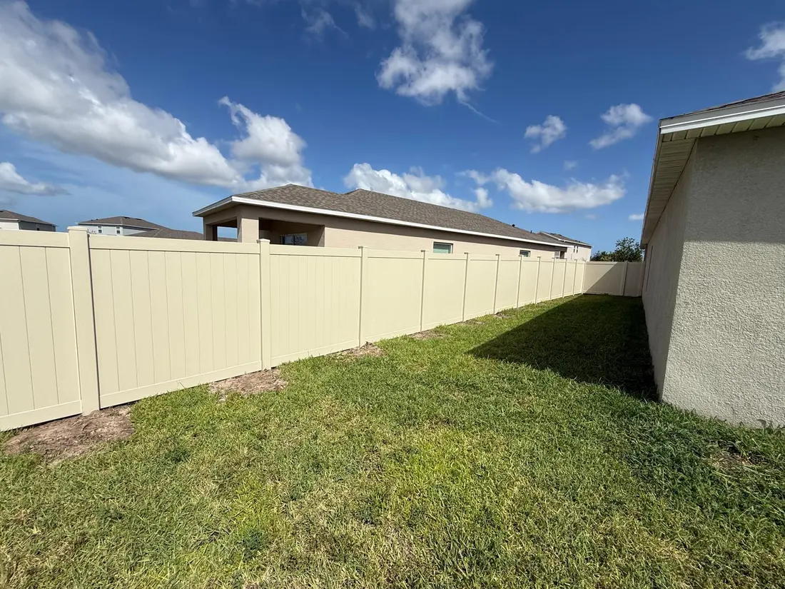Tan vinyl privacy fence along a new-construction backyard